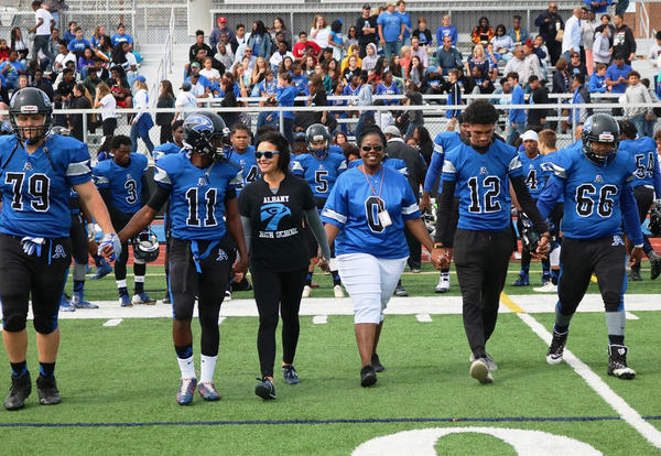 Superintendant Kaweeda G. Adams, ʿ High Principal Jodi Commeford and varsity football players walk hand-in-hand prior to the 2018 Homecoming game.