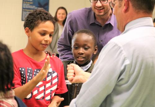 A student and teacher play Rock, Paper, Scissors while another student looks on.