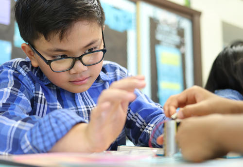 Student peering over his glasses as he works on building a circuit with a lightbulb and battery.