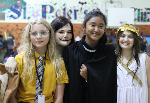 Three students posing for a picture with a teacher, and all four are wearing costumes.