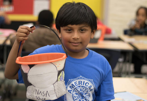 Smiling boy holds up decorated plastic pumpkin