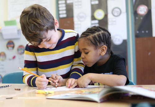 Two students working at their desk, reading and writing.