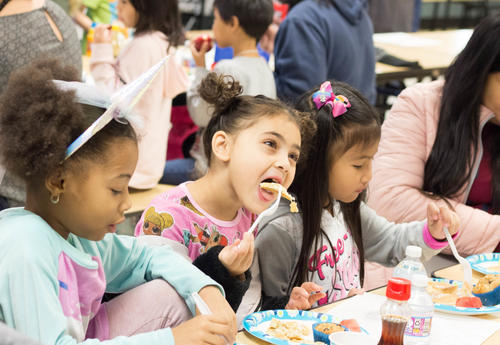 Three first-grade girls eat pancakes while wearing their pajamas