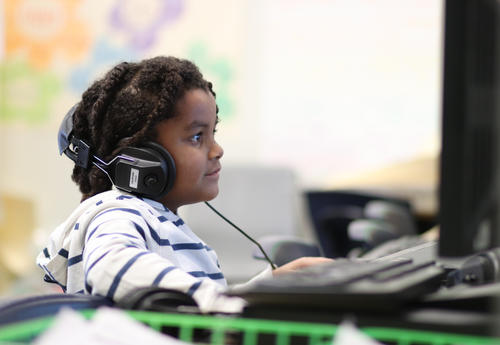 Student working at a computer smiling and wearing headphones.