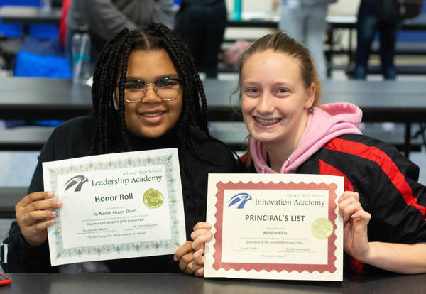 Two young women hold up the certificates they earned for Honor Roll and Principal's List