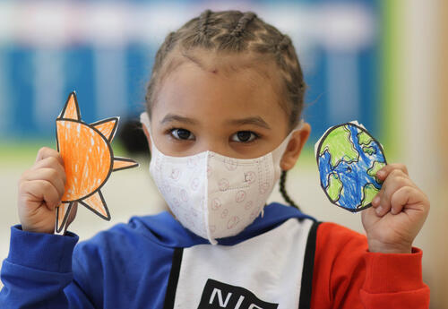 Masked student holding up paper cutouts of the sun and earth