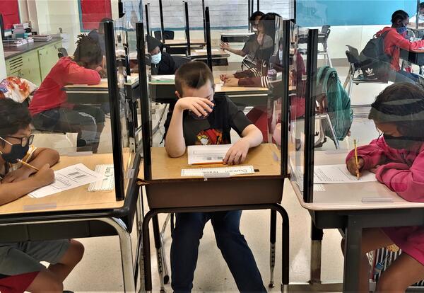 Students working at a desk surrounded by plastics dividers