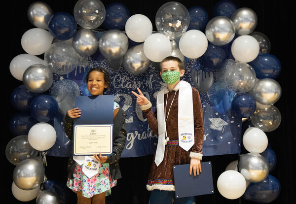 Two fifth graders pose with certificates in front of a Class of 2022 banner