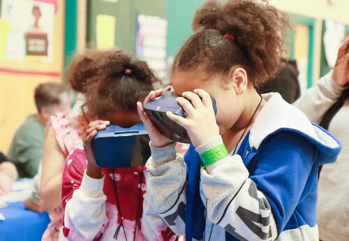 Two students peer through virtual reality goggles