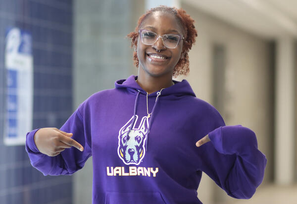 Senior smiling and pointing to their UAlbany sweatshirt