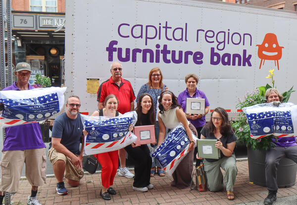 Ten people stand in front of a HATAS truck holding pillows, sheets and mattress pads