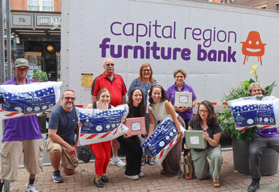 Ten people stand in front of a HATAS truck holding pillows, sheets and mattress pads