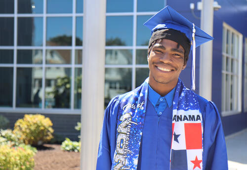 Photo of graduate in cap and gown outside of Albany High school