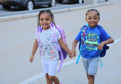 A brother and sister walk in to their first day of kindergarten together.
