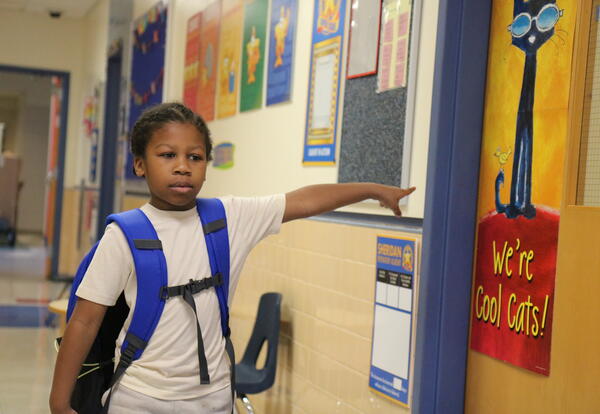 A kindergarten student points to the door of his classroom.