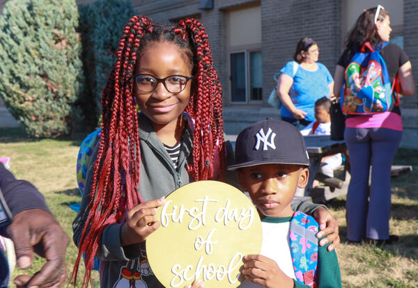 Girl and boy hold "first day of school" sign