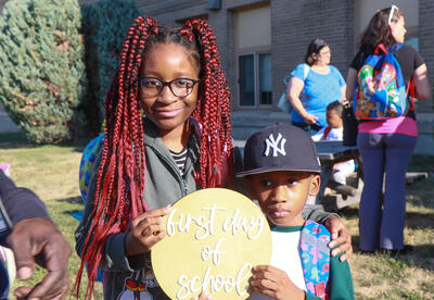 Girl and boy hold "first day of school" sign
