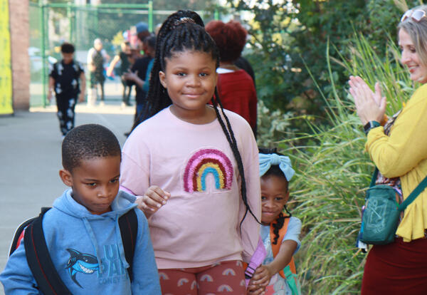 Three students walk through a corridor of cheering people