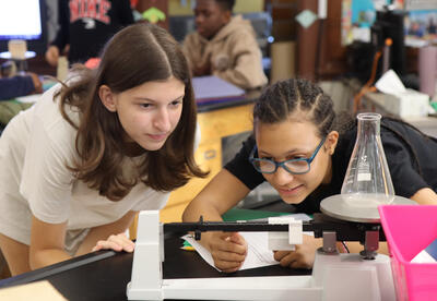 Two students adjust the levers on a triple-beam balance