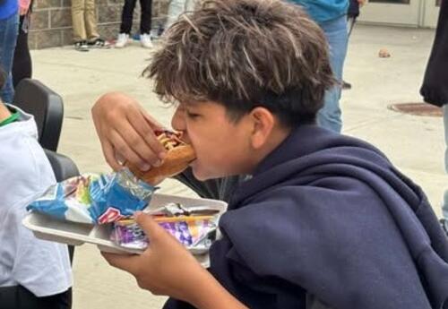 A student enjoys a hotdog during a BBQ.