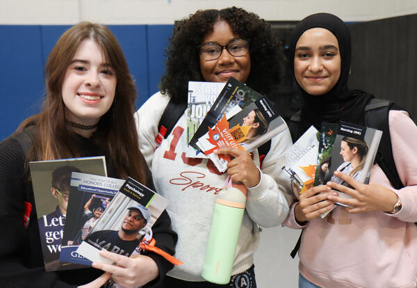 Group of three students at college fair holding brochures