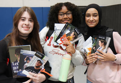 Group of three students at college fair holding brochures