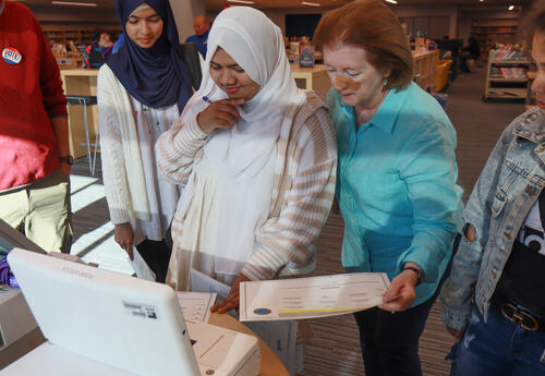 A student putting a mock ballot into a counting machine with the help of a volunteer from the League of Women Voters