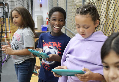 Three students use I-pads to operate robotic cars