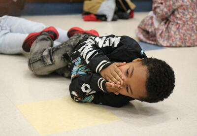 A student practices stop-drop-roll with help from the fire department.