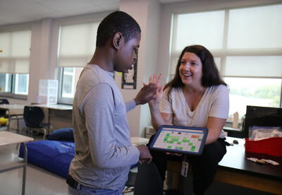 A student uses Augmentative and Alternative Communication to share information with a teacher.