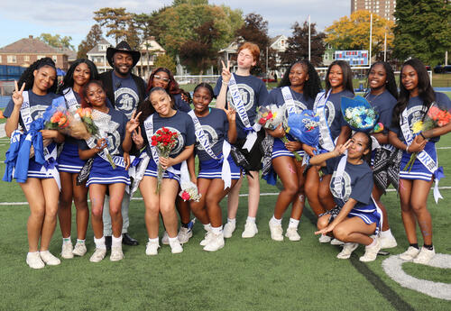 Seniors on cheerleading team posing together on the turf with Coach Jahmere Holland