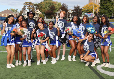 Seniors on cheerleading team posing together on the turf with Coach Jahmere Holland