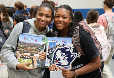 Two students at college fair event with college brochures