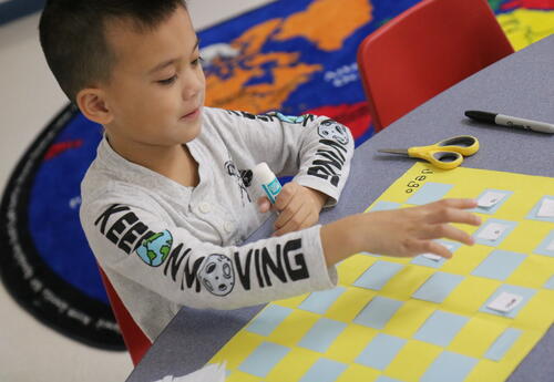 A student glues sight words on a placemat.
