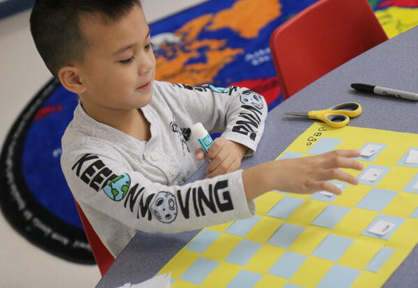 A student glues sight words on a placemat.