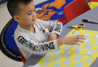 A student glues sight words on a placemat.