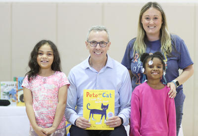 Eric Litwin posing for a photo with his book, two students, and Ms. Panton