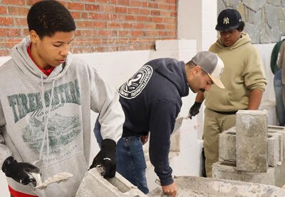 Two students working with a mason learning how to lay cement blocks