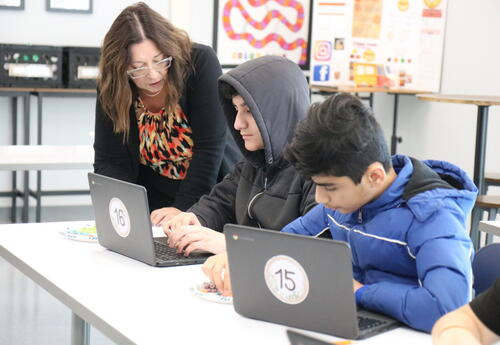 A teacher helps students with a lab on computers.