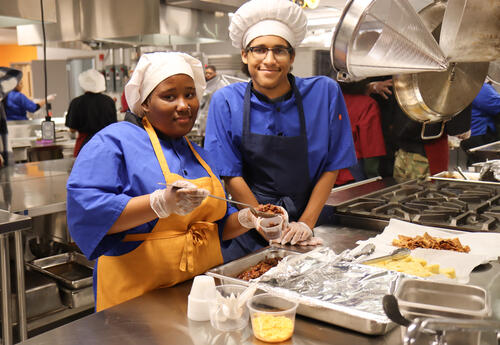 Two culinary students serving up a portion of chili at the cookoff event