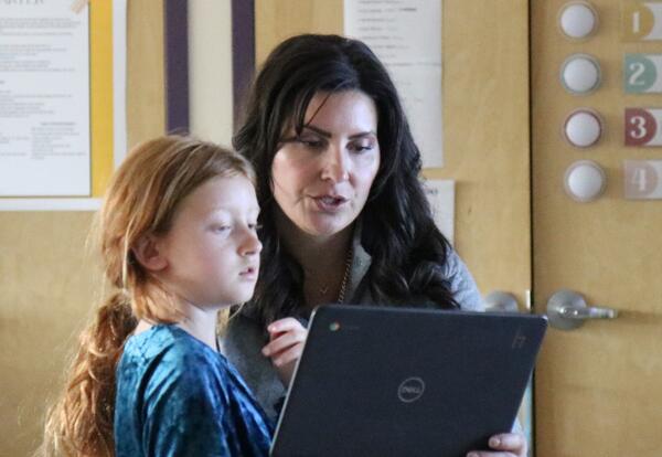 A teacher assists and student with an AI assignment.