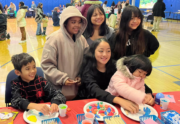 Two students seated at a table with their mom work sort shapes on paper plates
