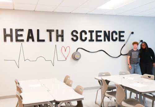 Verhoff and Blake posing with the artwork in the Health Sciences classroom