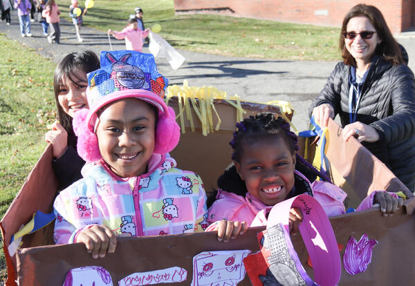 Three students march in their hand-made float while teacher looks on