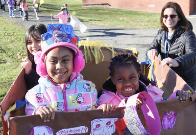 Three students march in their hand-made float while teacher looks on