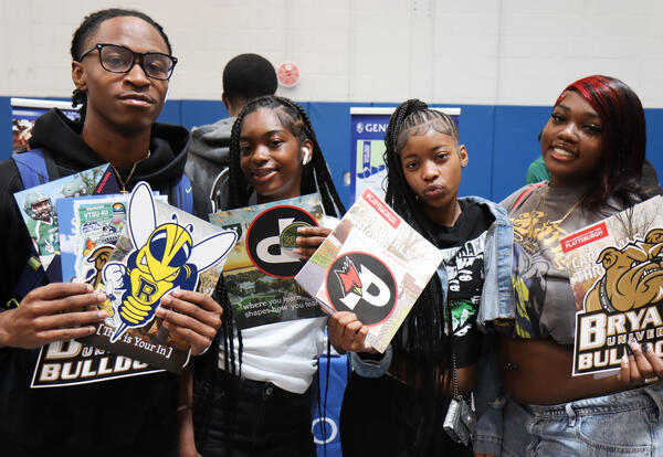 Group of four students at college fair event with college brochures