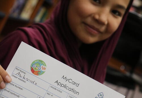 A students proudly shows her library card.