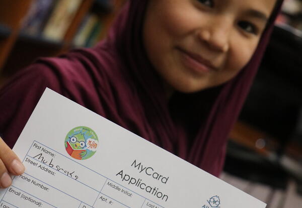 A students proudly shows her library card.