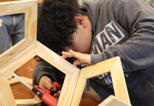 Student uses a glue gun to attach pieces of wood