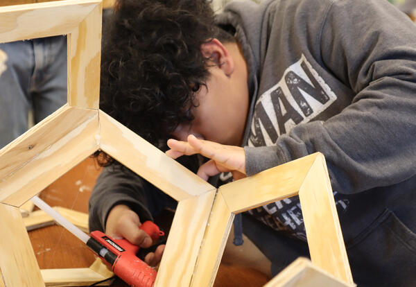 Student uses a glue gun to attach pieces of wood